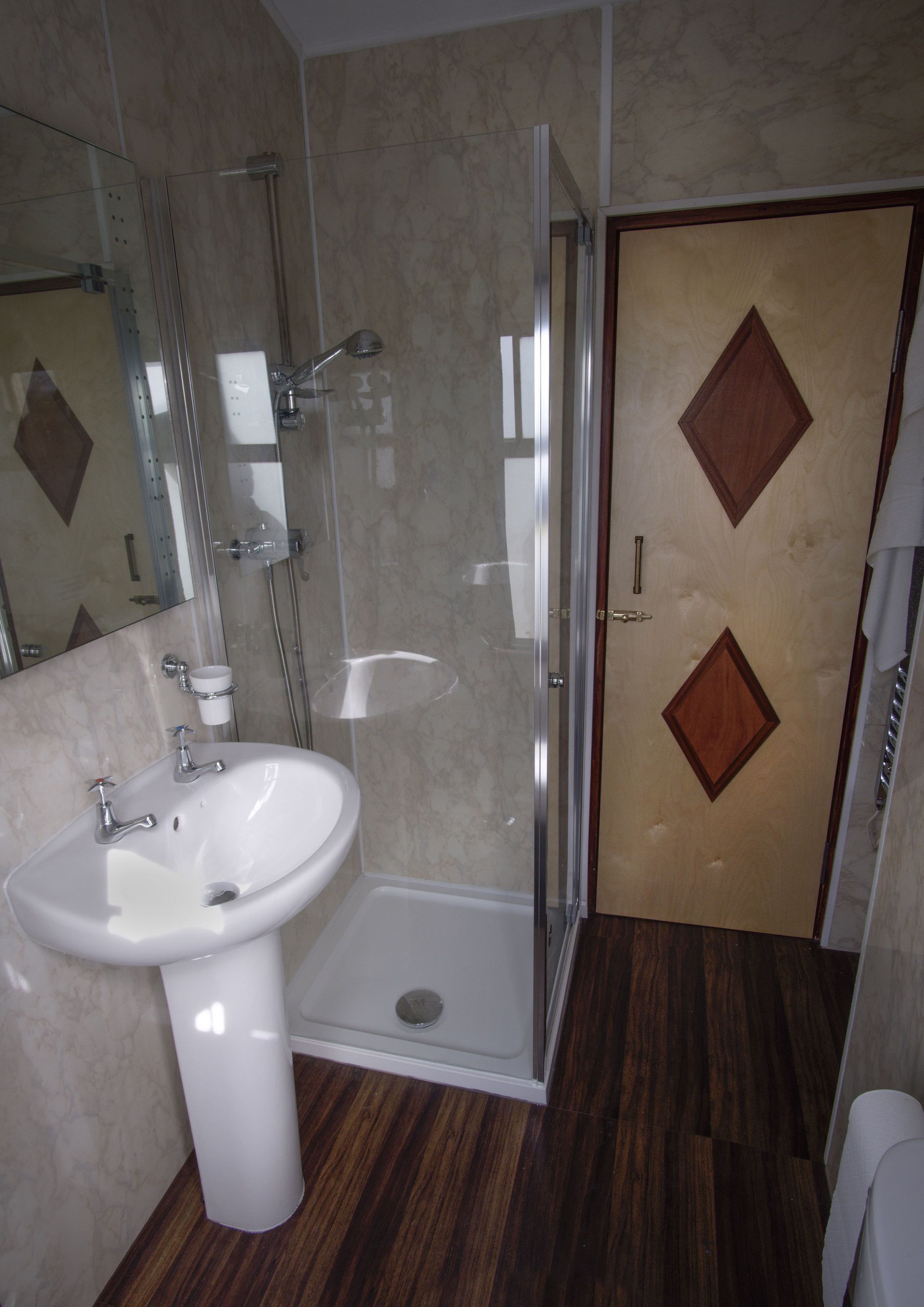 1 of two single beds found in the second room. It is under a window with curtains, a bedside table is beside it with a lamp and fan.